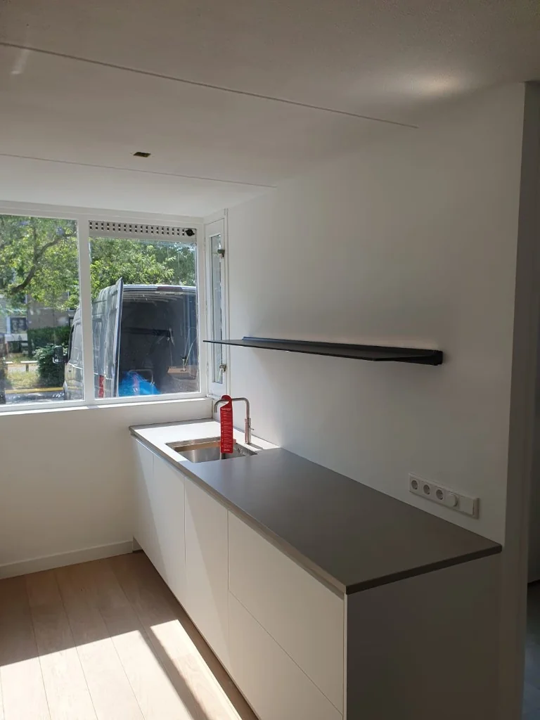 Lichte keuken met spoelbak en plank tegen witte wand